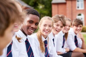 Students in uniforms sitting and smiling outdoors.