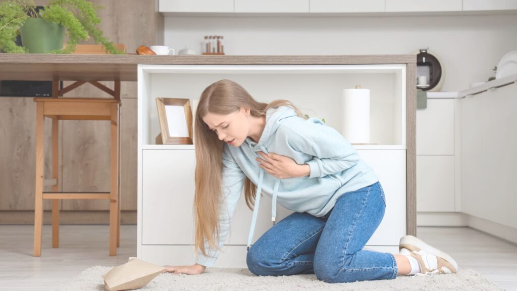 Woman clutching chest while kneeling in kitchen